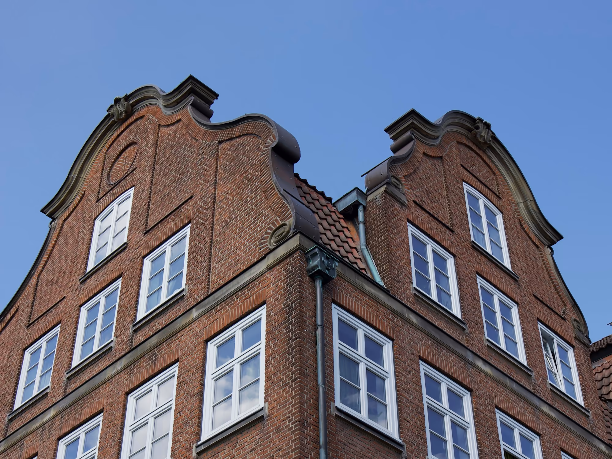 Hamburger Backsteinfassade mit geschwungenen Giebeln und weißen Sprossenfenstern vor blauem Himmel