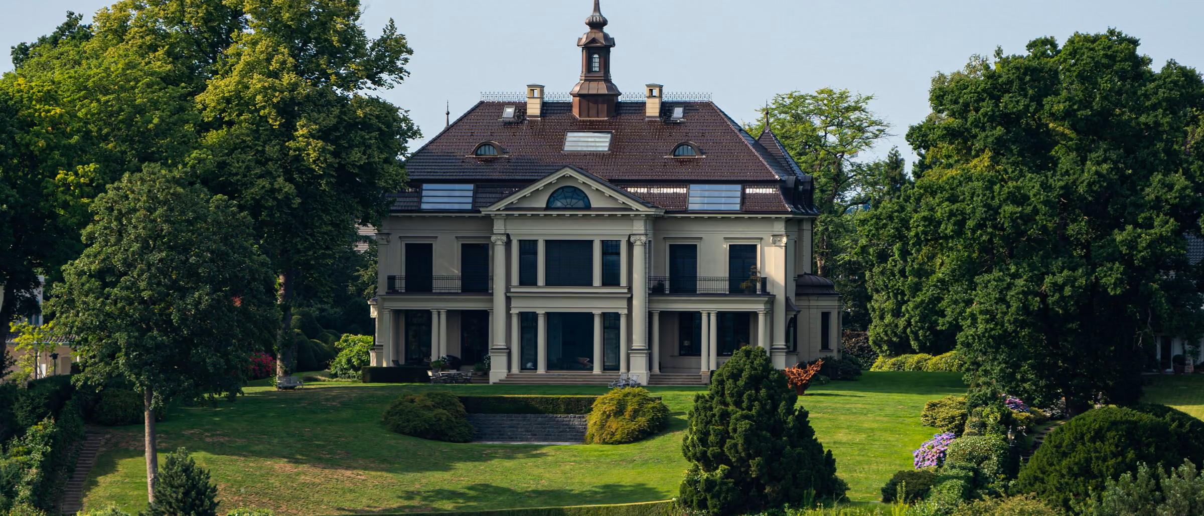 Villa in einem Park mit Rasenfläche und alten Bäumen oberhalb eines Wasserufers in Hamburg